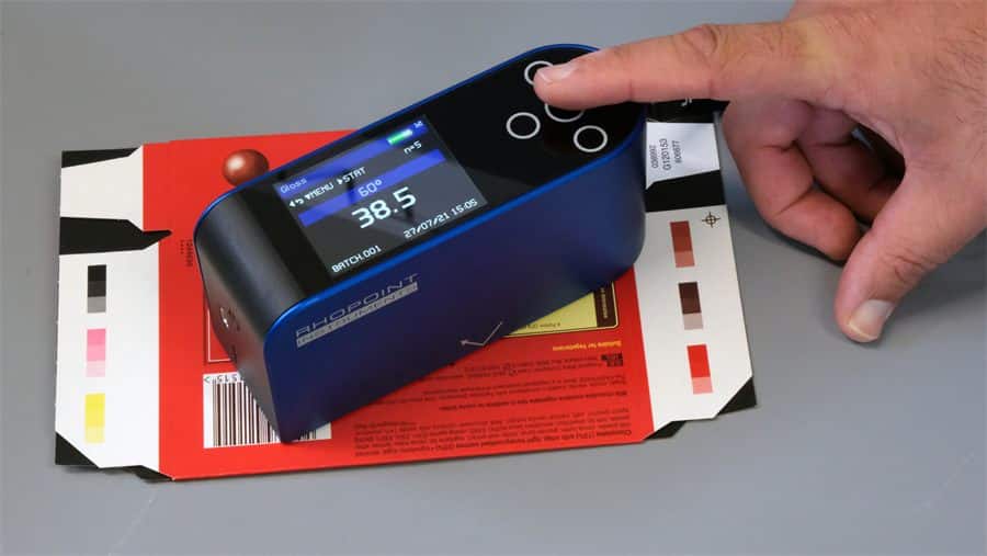 A Novo-Gloss glossmeter held in one hand, measuring the gloss of a press-printed carton